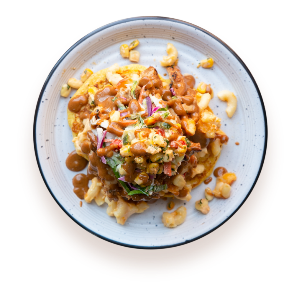 Overhead view of corn cakes, mac 'n' cheese, and pulled chicken stacked on a white plate